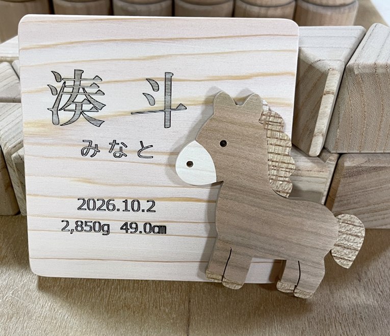 名前と生年月日を刻んだ木のプレートと、馬の飾り